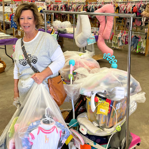 A young JBF shopper mom in a black Metallica T-shirt holds an outfit she intends to buy at her local JBF sale.