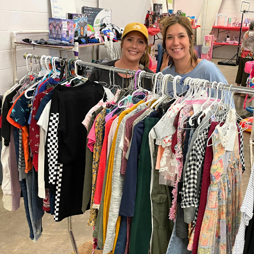 Two women with rack of clothing at a JBF sale. 